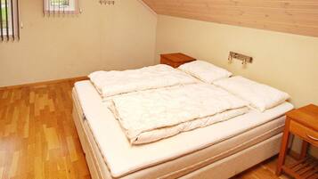 Un dormitorio con una cama grande, suelo de madera, una ventana pequeña y un cabecero de madera.