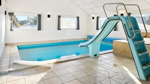 Una piscina interior con tobogán, suelo de baldosas y ventanas.