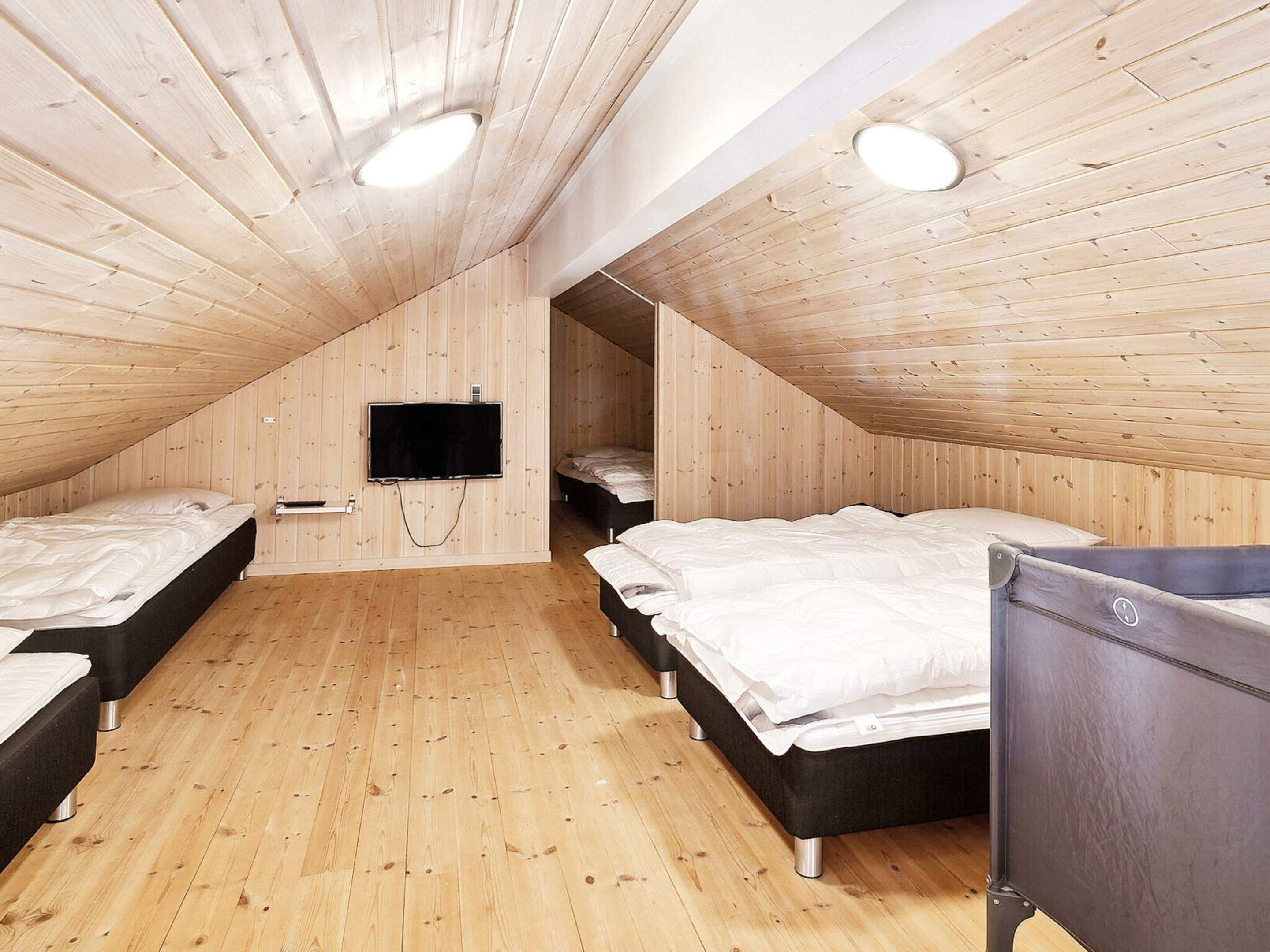 A room with wooden sloped ceilings, a flat-screen TV mounted on the wall, and three beds arranged in a row.