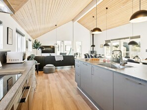 A modern kitchen with a wooden ceiling, a built-in oven, a sink, and a dining area with a sofa and chairs. - 5 Star Holiday Home in Harboore (Harboore)
