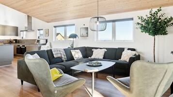 En moderne stue med et køkken, en stor sofa, to lænestole og et spisebord.