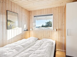 A single bed with white bedding in a room with wooden walls and a window.