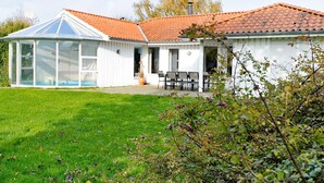 Uma casa com uma estufa de vidro, um alpendre com móveis de exterior e um relvado bem cuidado.
