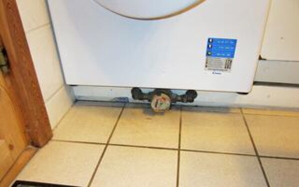 A white water heater with a control panel, located in a tiled bathroom.