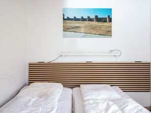 A bedroom with a bed, a headboard, a wall-mounted picture, and a power outlet.