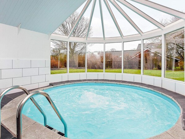 A swimming pool with a glass enclosure, surrounded by a white tiled wall and large windows.
