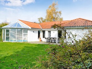 A house with a glass conservatory, a patio with outdoor furniture, and a well-maintained lawn. - 4 Star Holiday Home in Juelsminde (Horsens)