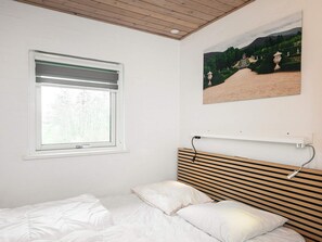 Une chambre à coucher avec un lit, une fenêtre avec des stores, une étagère fixée au mur et un tableau représentant un paysage.