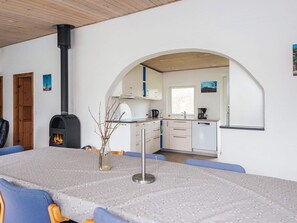 A modern kitchen with a wood-burning stove, a dining area with a table and chairs, and an arched doorway leading to another room. - 4 Star Holiday Home in Juelsminde (Horsens)