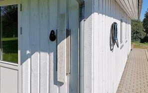 A white building with a window, a door, and a small outdoor area with a wheelchair.