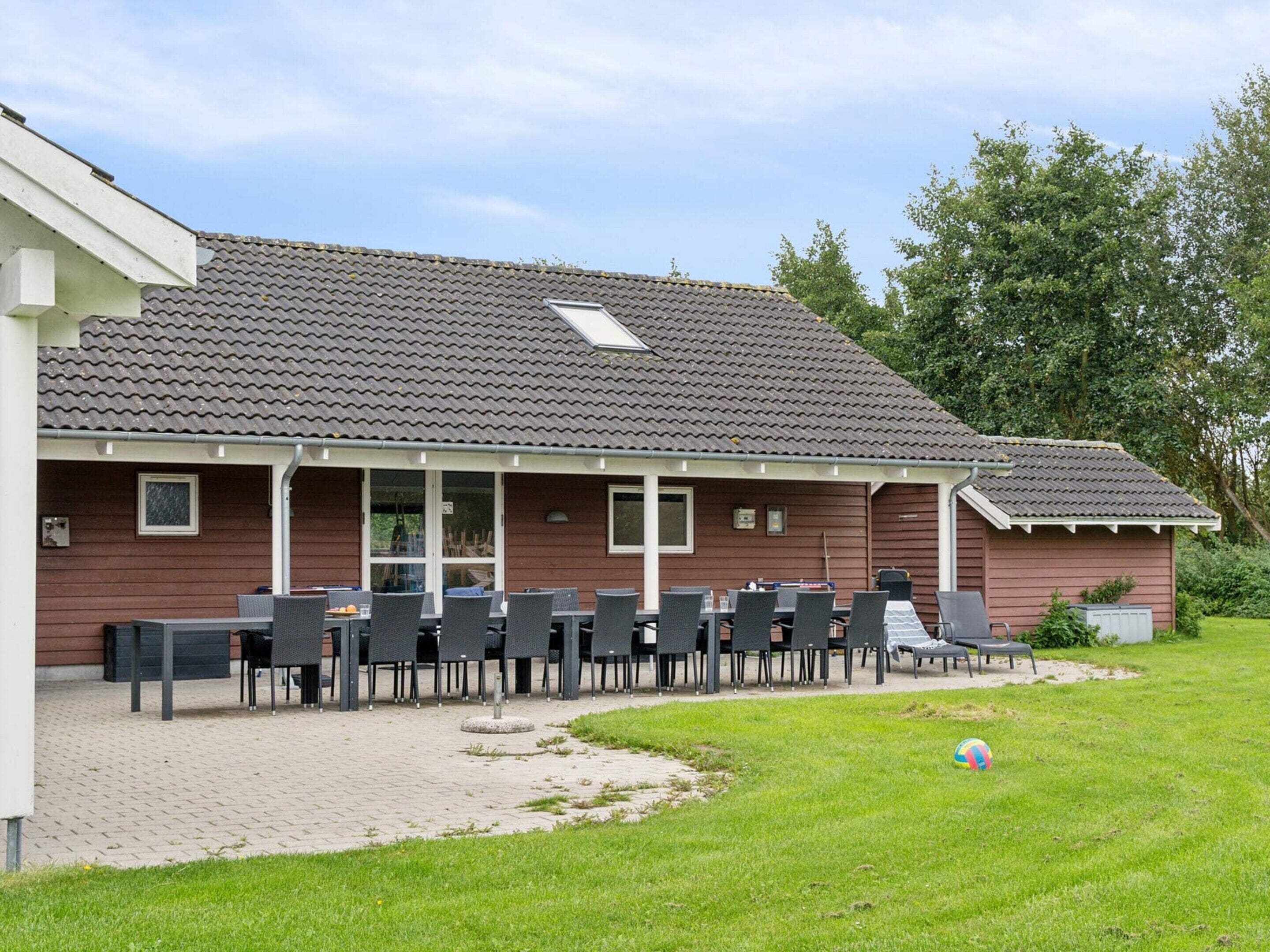 A building with a tiled roof, outdoor seating area with tables and chairs, and a grassy lawn.