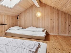 A room with a sloped ceiling, wooden walls, a bed with white bedding, and a single light fixture. - 5 Star Holiday Home in Idestrup (Idestrup)
