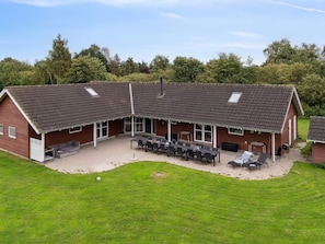 A two-story building with a covered patio area, multiple tables and chairs, and a lawn. - 5 Star Holiday Home in Idestrup (Idestrup)
