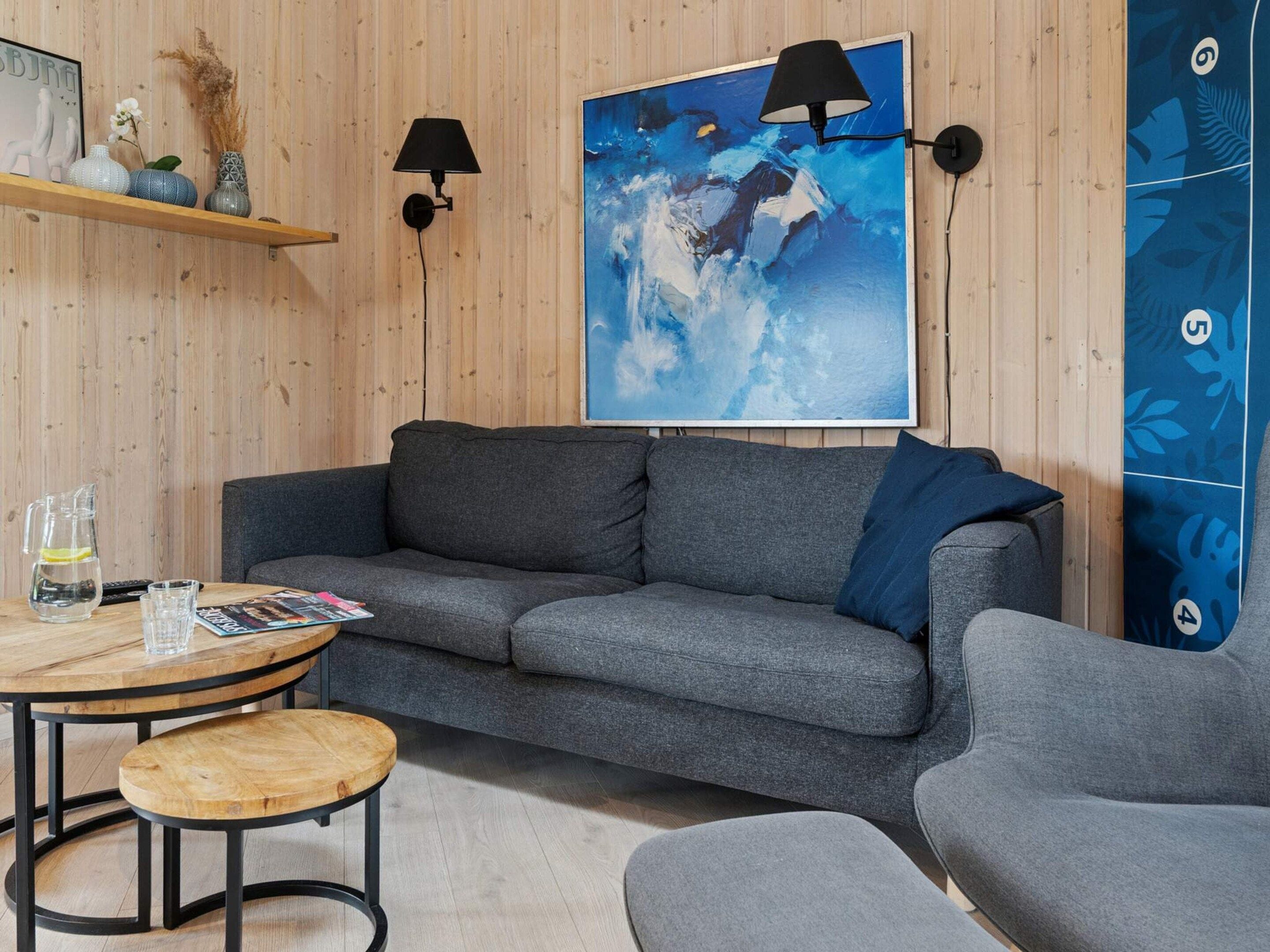 A modern living room with a grey sofa, a round wooden table, and a blue abstract painting.