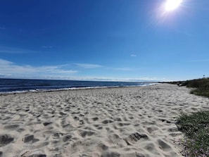 Praia arenosa com pegadas que levam à água, céu claro e horizonte distante.
