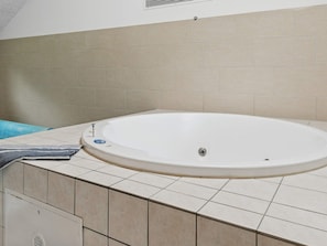A bathroom with a white bathtub, beige tiles, and a towel on the floor. - 5 Star Holiday Home in Idestrup (Idestrup)