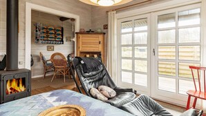 A cozy living room with a fireplace, a leather chair, a dining table, and a large window with a view of the outdoors. - 4 Person Holiday Home in Lokken (Lokken)