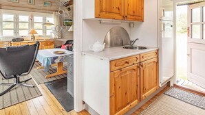 A kitchen with wooden cabinets, a sink, and a dining area with a table and chairs. - 4 Person Holiday Home in Lokken (Lokken)