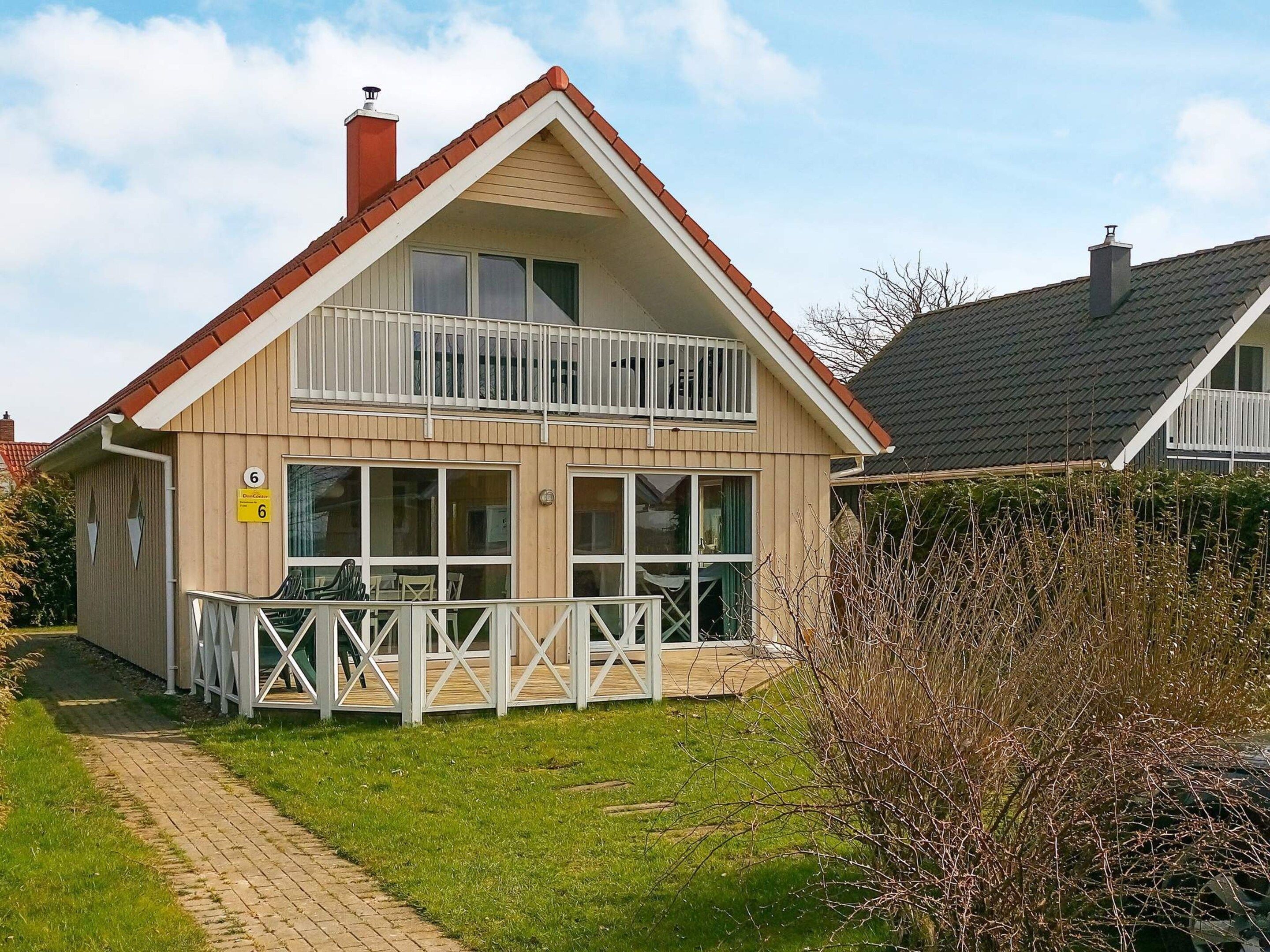 Une maison à deux étages avec un balcon, une enseigne portant le chiffre « 6 » bien visible, et une allée pavée.