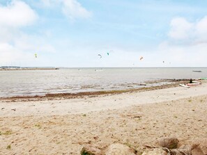 A beach with a sandy shore, a pier in the distance, and a person sitting on a surfboard. - Holiday Home in Gilleleje (Gelting)