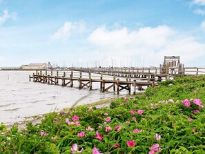 A pier with multiple wooden walkways extending into the water, surrounded by green vegetation and pink flowers. - Holiday Home in Gilleleje (Gelting)