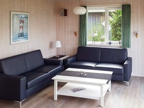 A living room with two black sofas, a white coffee table, a framed painting of a lighthouse, a lamp, and a window with curtains.