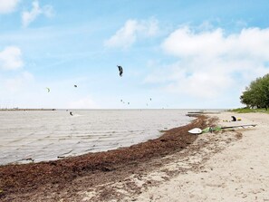 Une plage avec un rivage sablonneux, une jetée qui s’avance dans l’eau et une personne pratiquant le kitesurf.