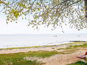 A beach with a sandy path leading to the water, a bench, and a boat in the distance. - Holiday Home in Gilleleje (Gelting)