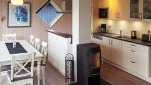 A modern kitchen with a wood stove, white cabinets, and a dining area with white chairs. - Holiday Home in Gilleleje (Gelting)