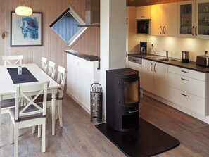 A modern kitchen with a wood stove, white cabinets, and a dining area with white chairs.
