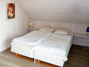 A bedroom with a wooden sloped ceiling, a double bed with white bedding, a bedside table with a lamp, and a wall-mounted painting.