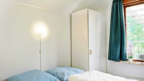 Ein Schlafzimmer mit zwei Betten, einem Kleiderschrank, einem Fenster mit Vorhängen und einer Wandleuchte.