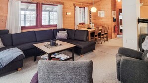 A cozy log cabin interior with a dark-colored sofa, a wooden dining table, and a fireplace. - 6 Person Holiday Home in Aseral (Aseral)