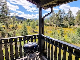 Un balcón con una parrilla, con vista a un paisaje boscoso y montañas a lo lejos.
