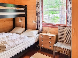 Una habitación de madera con una cama, un tocador, una silla y una ventana con vistas a la vegetación.