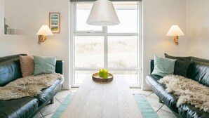 Ein modernes Wohnzimmer mit zwei Ledersofas, einem Holztisch und einem großen Fenster mit Blick.