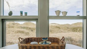 Ein Korbwesen mit einer blauen und weißen Keramikkanne auf einem Tisch, mit Blick auf eine grüne Landschaft durch ein Fenster.