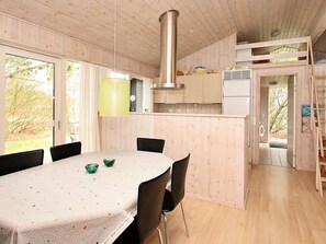 A wooden interior with a dining table, chairs, a kitchen area, and a staircase.