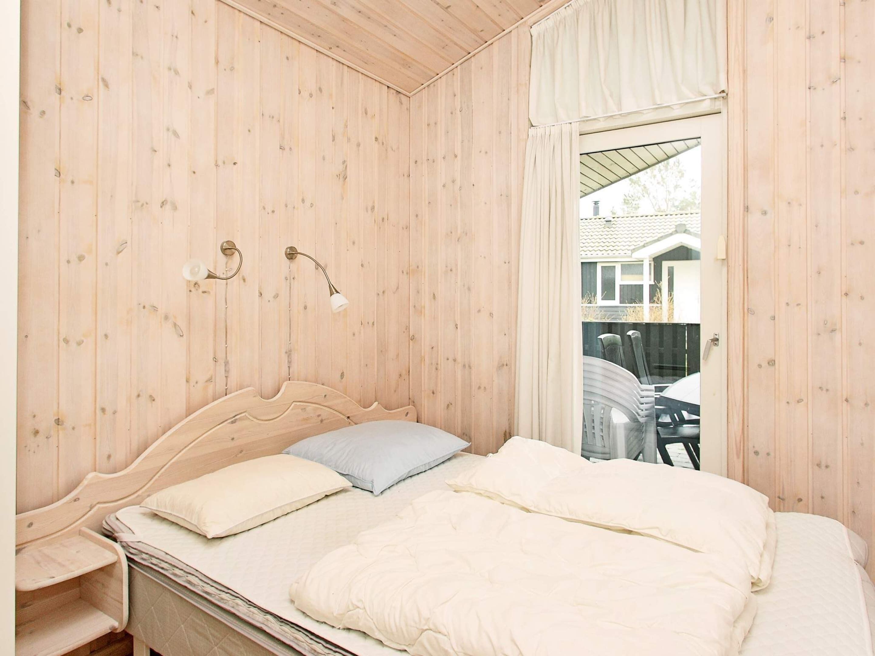 Quarto com painéis de madeira, uma cama, duas luminárias de cabeceira e uma janela com cortinas.