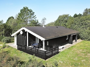 A single-story building with a black roof and white trim, surrounded by a wooden fence and greenery. - 4 Star Holiday Home in Albaek (Aalbaek)