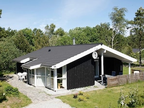 A single-story house with a black exterior, a sloped roof, and a covered porch with chairs.