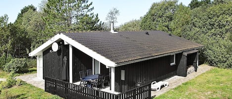 A single-story building with a black roof and white trim, surrounded by a wooden fence and greenery.