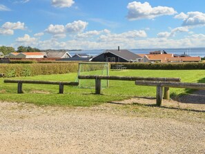 A gravel path leading to a fenced area with a bench, a soccer goal, and houses in the background.