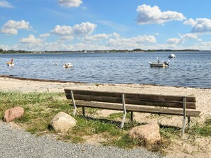 A bench by a lake with boats and a distant shoreline. - 4 Star Holiday Home in Sjolund (Sjølund)