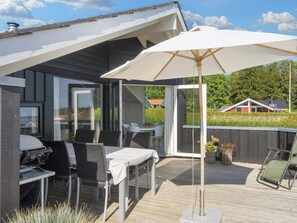 An outdoor patio with a table and chairs, a grill, and a large umbrella. - 4 Star Holiday Home in Sjolund (Sjølund)