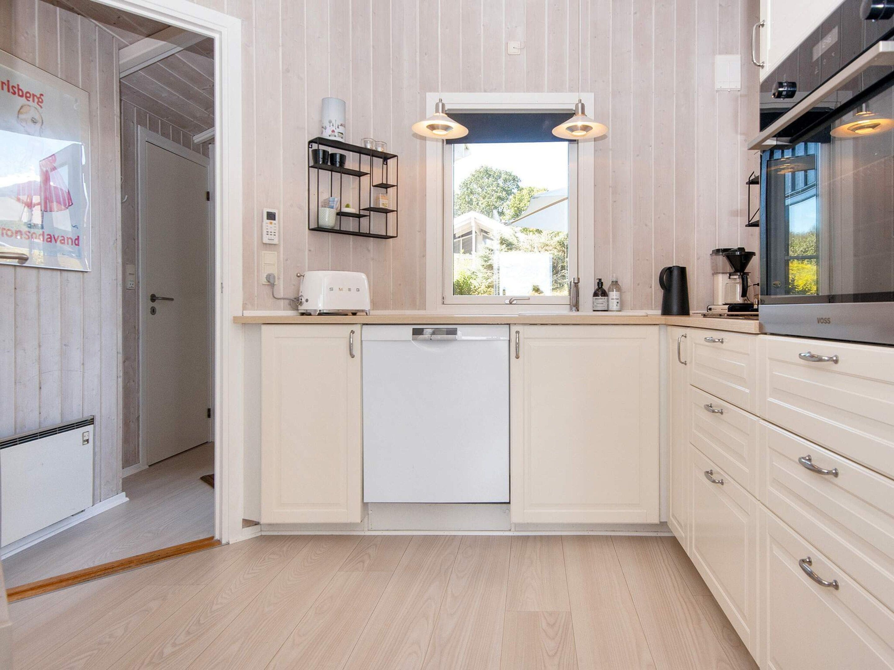 A modern kitchen with white cabinetry, a built-in dishwasher, and a window providing natural light.