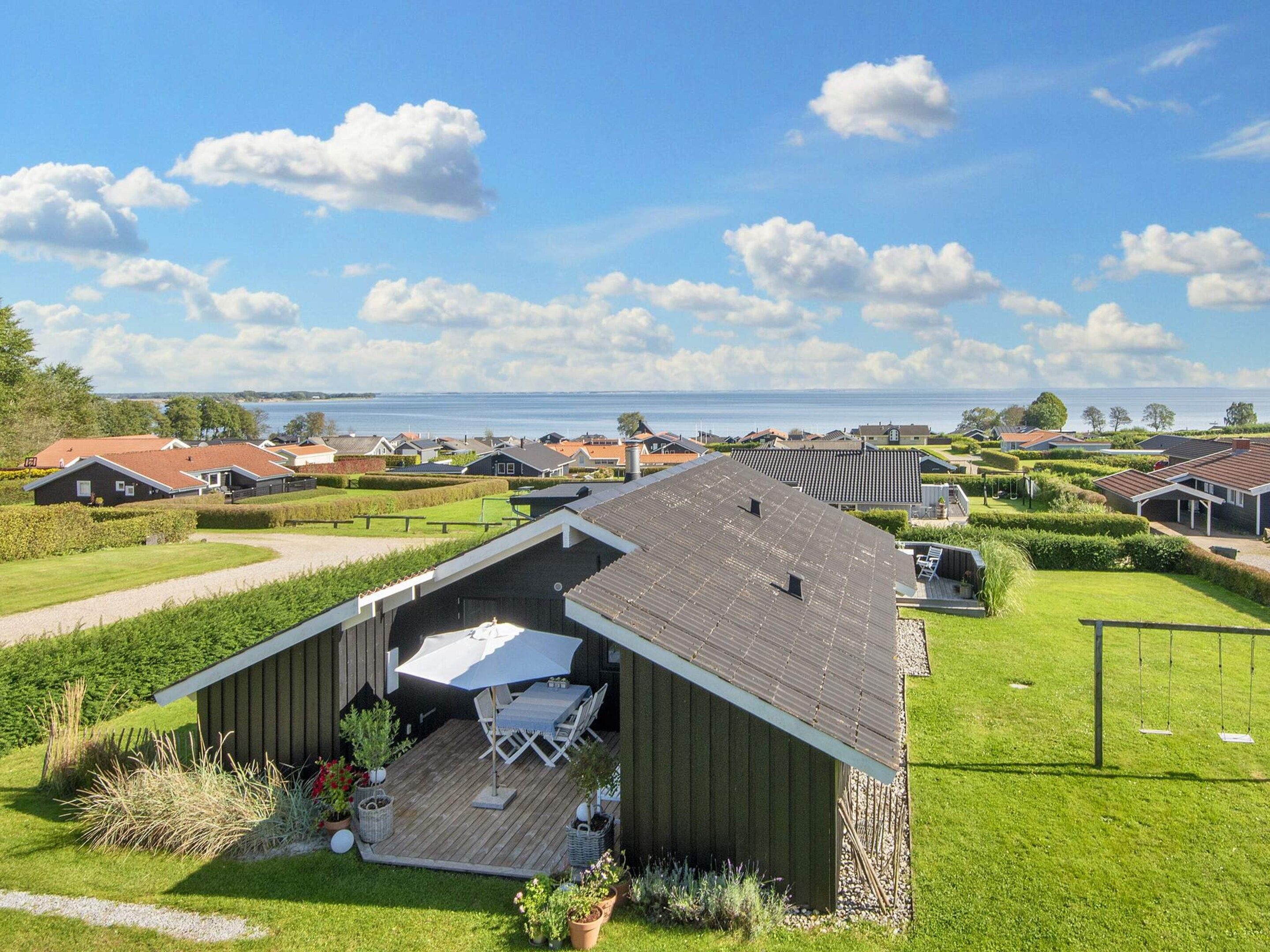 A residential area with houses, a wooden deck with outdoor furniture, and a view of the sea.