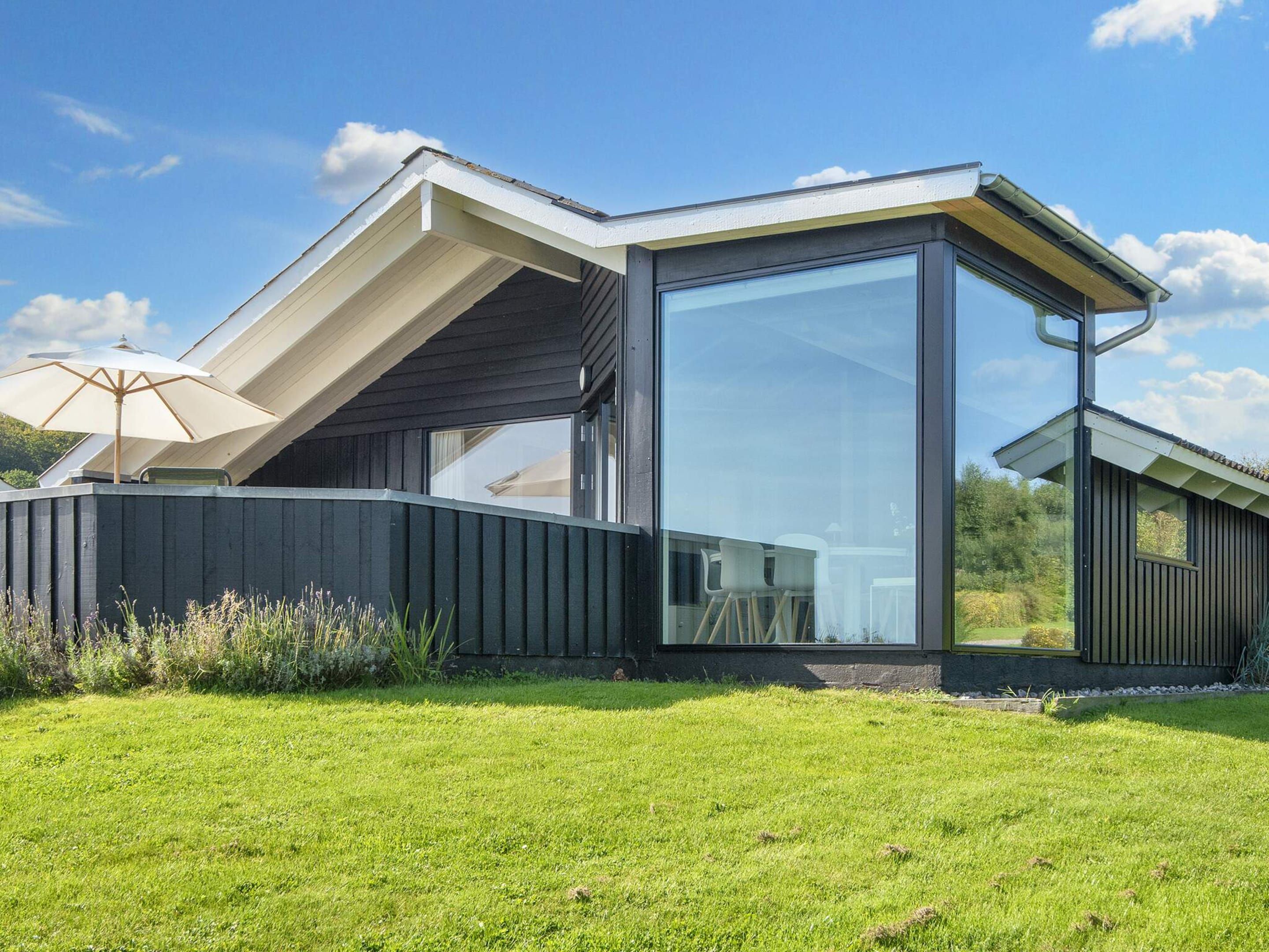 A modern house with a large glass window, a curved roof, and a grassy yard.