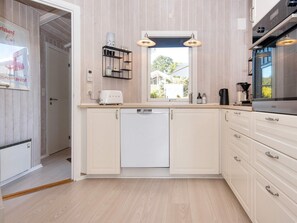 A modern kitchen with white cabinetry, a built-in dishwasher, and a window providing natural light. - 4 Star Holiday Home in Sjolund (Sjølund)