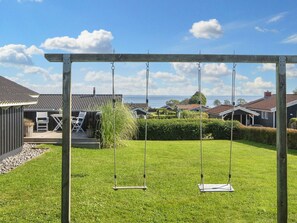 A wooden swing set in a grassy yard with a view of houses and the sea in the background. - 4 Star Holiday Home in Sjolund (Sjølund)